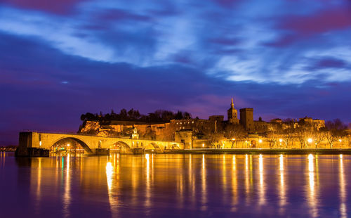 Illuminated buildings by river against sky at night