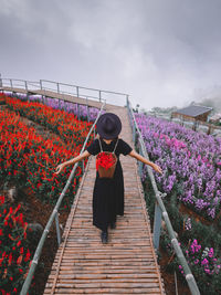 Rear view of woman walking on footbridge against sky