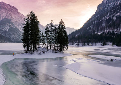 Person standing on frozen sea against trees and mountains