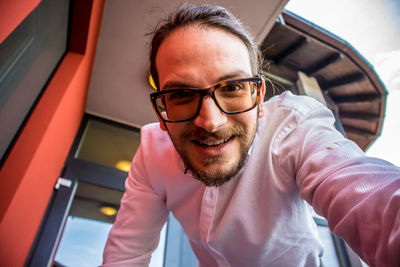 Low angle portrait of man wearing eyeglasses against building