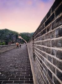 Rear view of people walking on walkway against sky during sunset