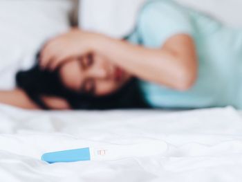 Close-up of pregnancy test equipment with woman relaxing in background on bed