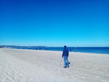 Rear view of man on beach against clear blue sky