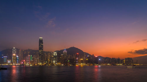 Illuminated buildings by bay against sky at night