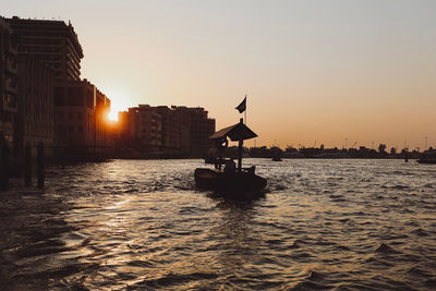 Silhouette buildings by sea against sky during sunset