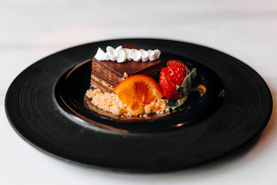 Delicious dessert chocolate piece of cake with fresh strawberry and orange on a black plate