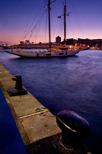 Sailboats moored in harbor at sunset