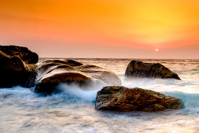 Scenic view of rocks in sea against sky during sunset