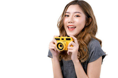 Portrait of smiling woman holding camera over white background