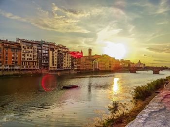 River by buildings against sky during sunset