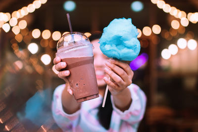 Close-up of woman holding cold coffee and cotton candy outdoors at night