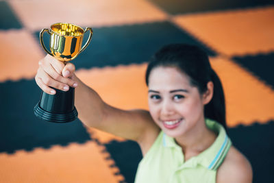 Portrait of young woman holding trophy while standing on tiled floor
