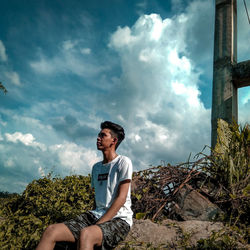 Young man sitting on land against sky