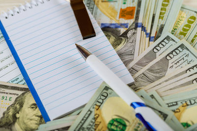 Close-up of pen with blank notepad on currency