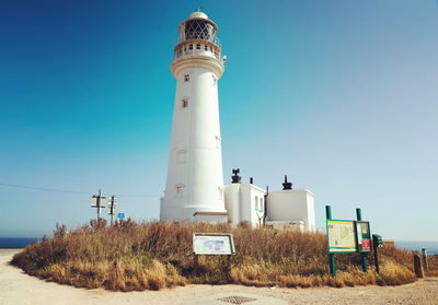 Lighthouse on field against clear blue sky