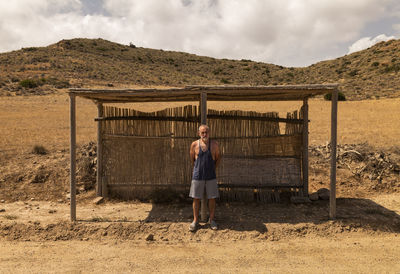 Full length portrait of adult man waiting bus in a wooden bus stand in nature park in summer