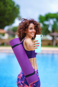 Vertical view of curly hair woman dressed in a yoga outfit holding bottle of water, focus on bottle