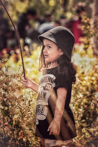 Cute girl with stick standing by plants