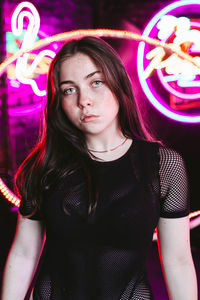 Portrait of beautiful young woman standing against illuminated lights