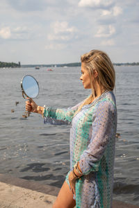 Side view of woman holding hand mirror at beach