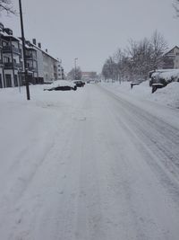 Snow covered road by buildings against sky