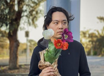 Young asian man holding bunch of tulips against trees at sunset