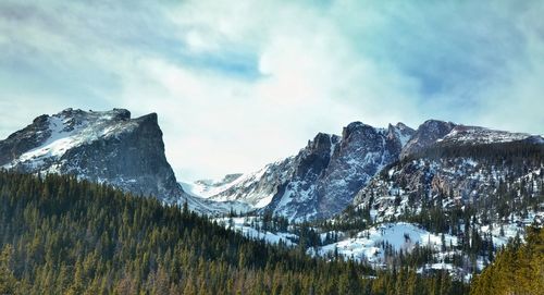 Low angle view of snowcapped mountains and trees against cloudy sky