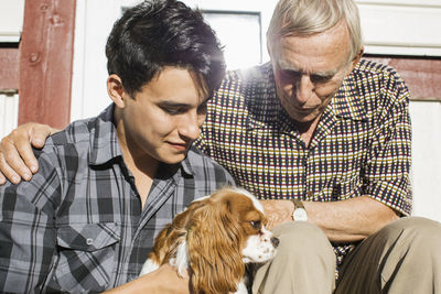 Grandson and grandfather looking at dog outside house