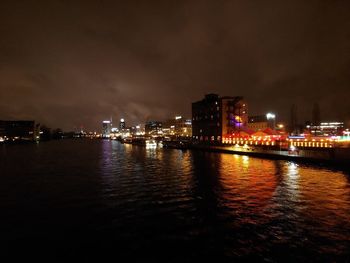 Illuminated buildings by river against sky at night