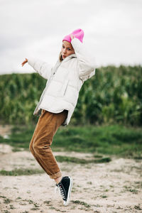 Cheerful beautiful teenage girl in a yellow raincoat and a pink hat is dancing on the background 