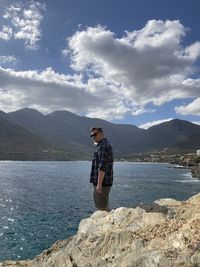 Man standing on rock by lake against sky