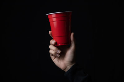 Close-up of hand holding coffee cup against black background