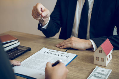 Midsection of real estate agent giving house key to customer at office