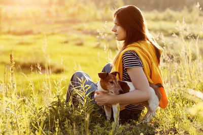 A beautiful young girl is sitting on the grass and hugging her dog. a girl and her pet are resting 