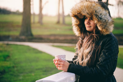 Young woman holding coffee cup while wearing warm clothes