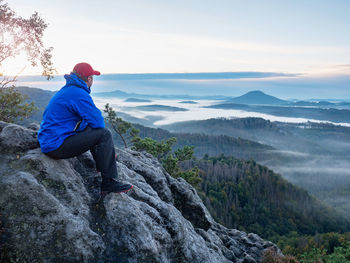 Hiker in blue jacket sit alone on the rock summit. wonderful daybreak view to heavy mist in valley
