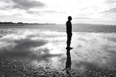 Reflection of man standing on beach against sky