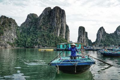 Woman rowing rowboat in sea against mountains