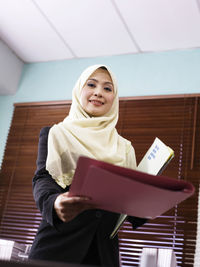 Portrait of businesswoman in hijab holding file at office