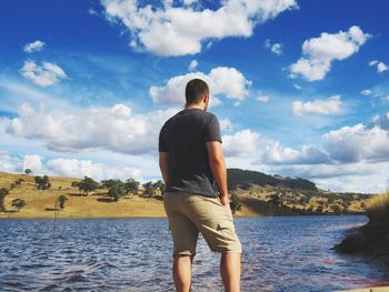 Rear view of man looking at lake against sky