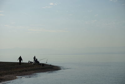 Silhouette men fishing by sea against sky