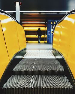 Rear view of man walking in building seen through escalator