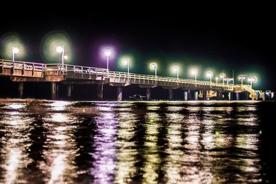 Illuminated bridge over river against sky in city at night