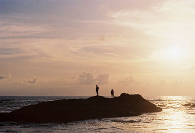 Silhouette men standing on sea against sky during sunset