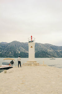 Beacon on pier by river against mountain against sky