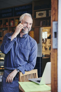 Sales clerk smiling while talking on mobile phone in deli