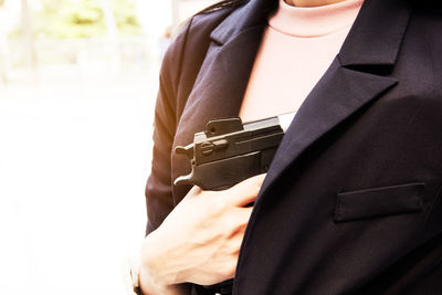 Midsection of woman holding gun inside blazer