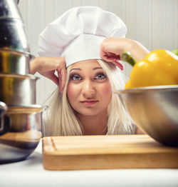 Portrait of young woman with head in hands standing in kitchen