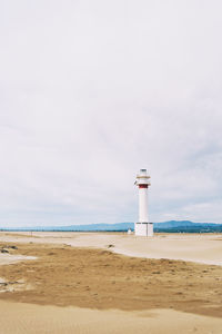 Lighthouse on beach by sea against sky