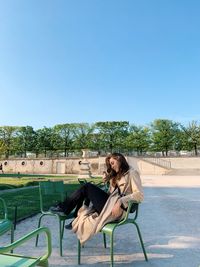 Side view of woman sitting on beach against clear blue sky
